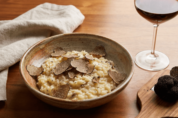 Risotto with wild porcini mushrooms and black truffles from Italy served in a plate close up on white table. Eating Italian gourmet cousine